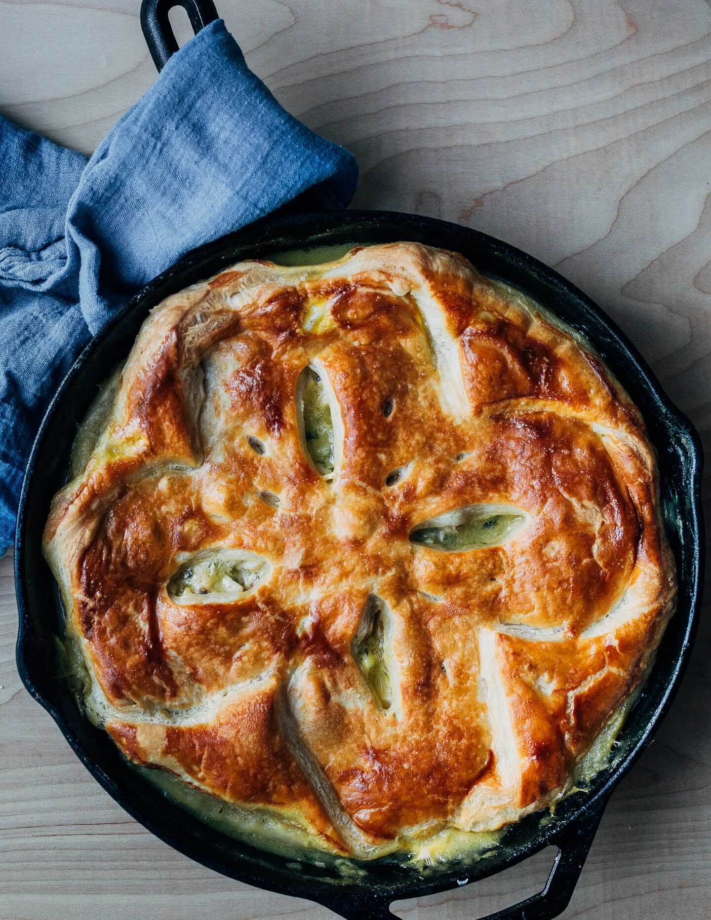 A skillet with a just-baked pot pie and a cloth around the handle. 