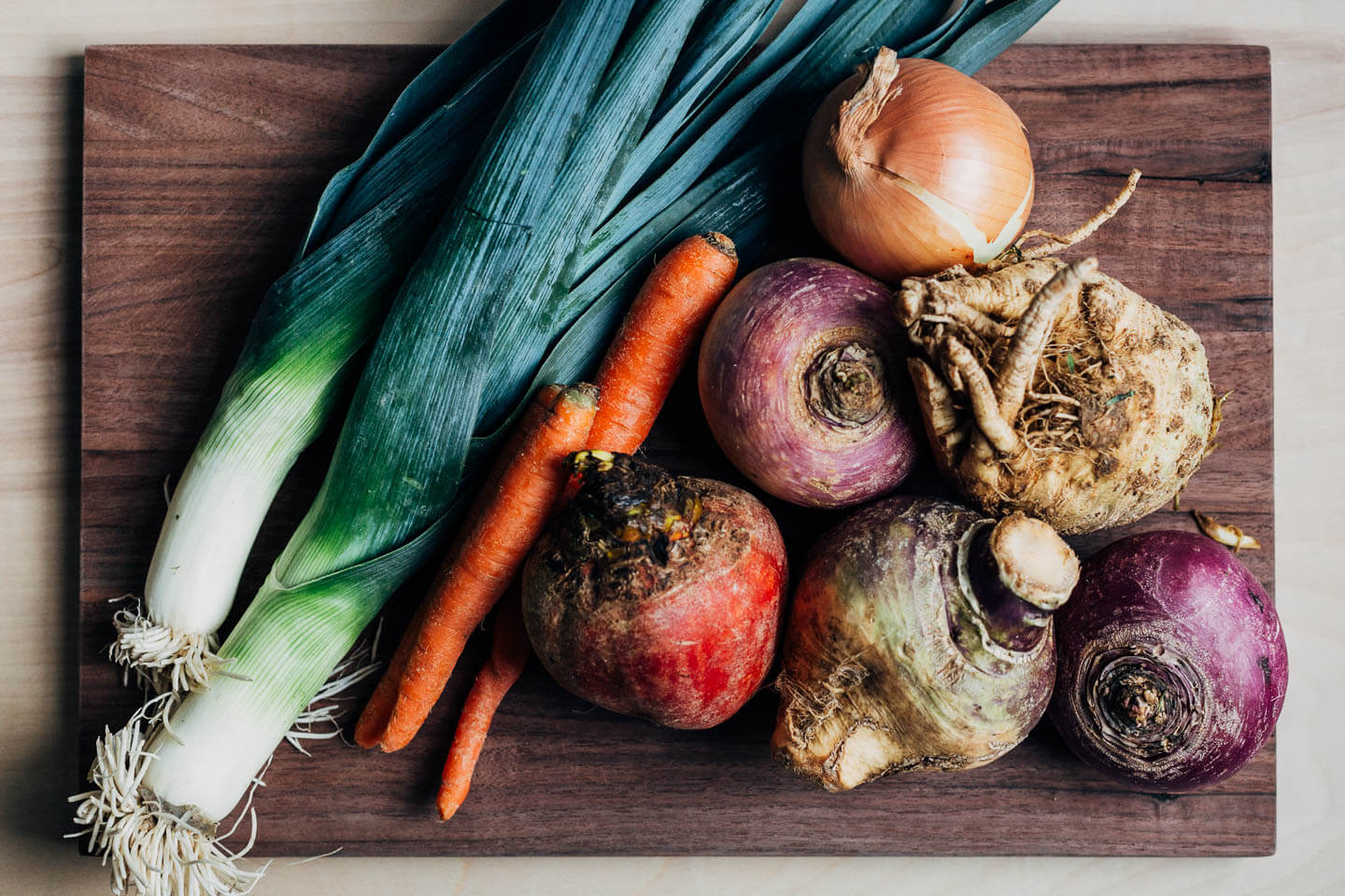 A cutting board with leeks and root vegetables