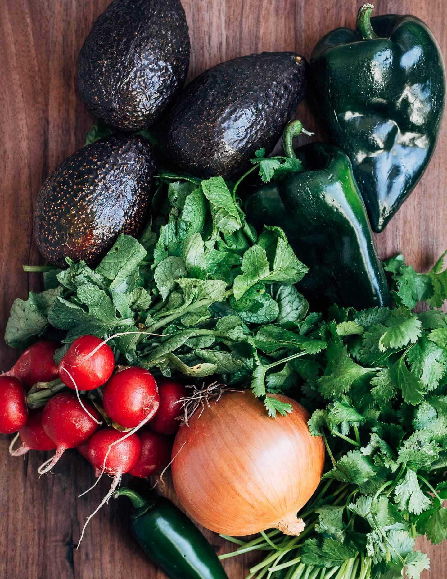 Fresh produce for tortilla soup on a cutting board. With radishes, onion, cilantro, poblanos, and avocados. 