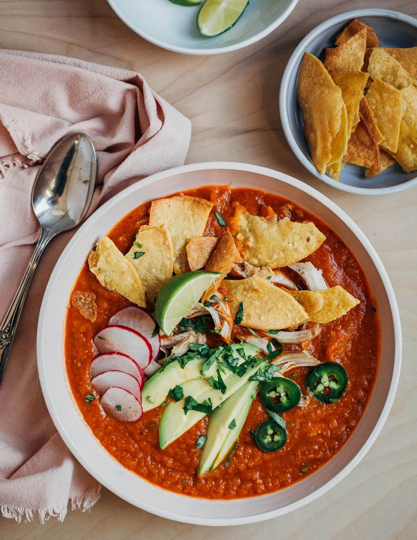 A bowl of tortilla soup topped with avocado, radishes, jalapeños, fried tortillas and chicken.