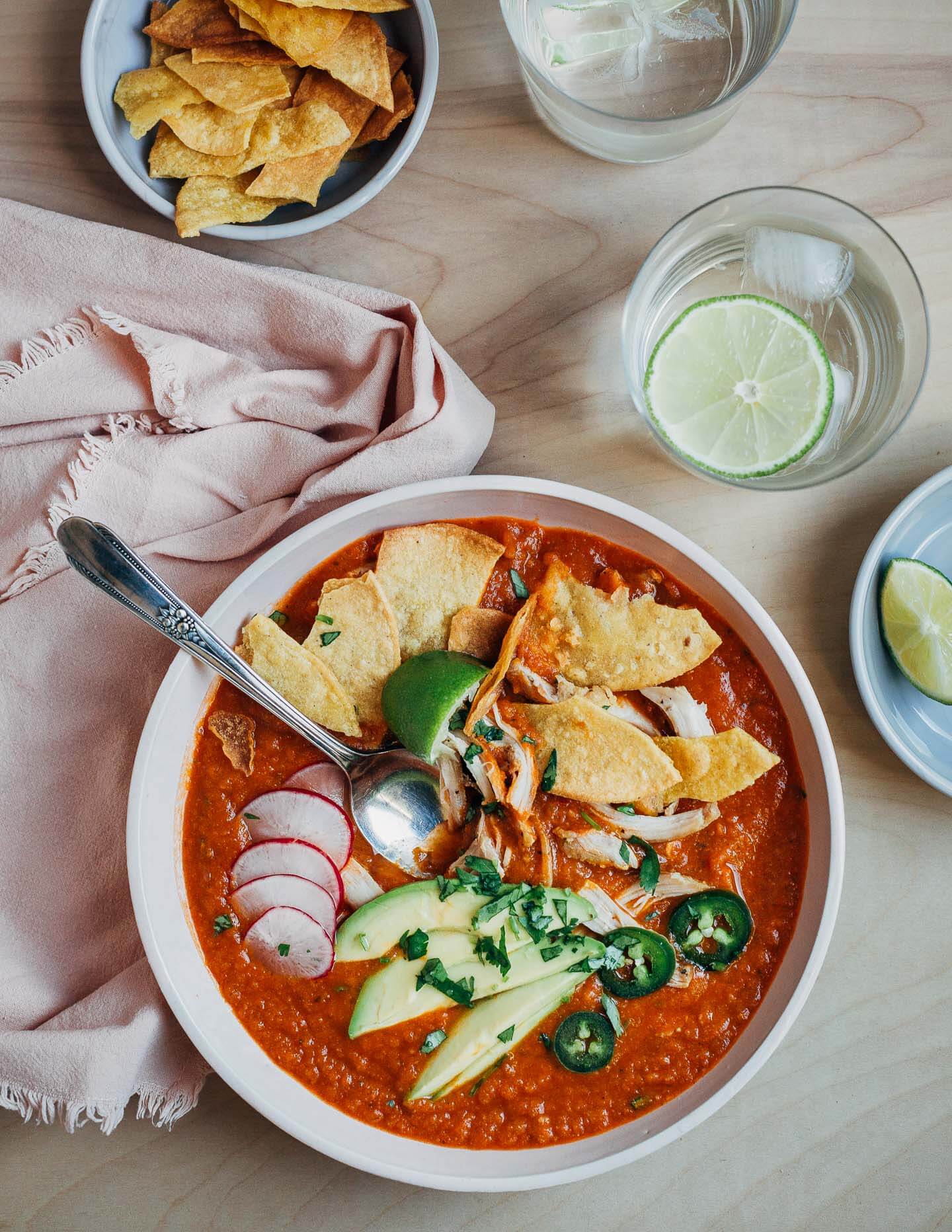 A bowl of tortilla soup topped with avocado, radishes, jalapeños, fried tortillas and chicken. 