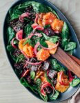 A platter with a colorful beet and citrus salad topped with sesame seeds. Salad tongs are alongside.