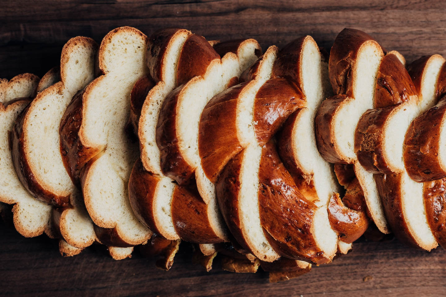 Sliced challah on a dark wood cutting board. 