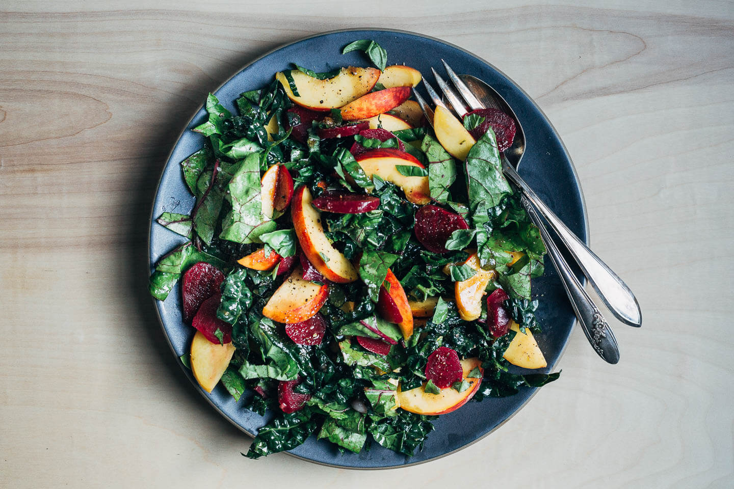 A platter with a tossed beet, peach, and greens salad.