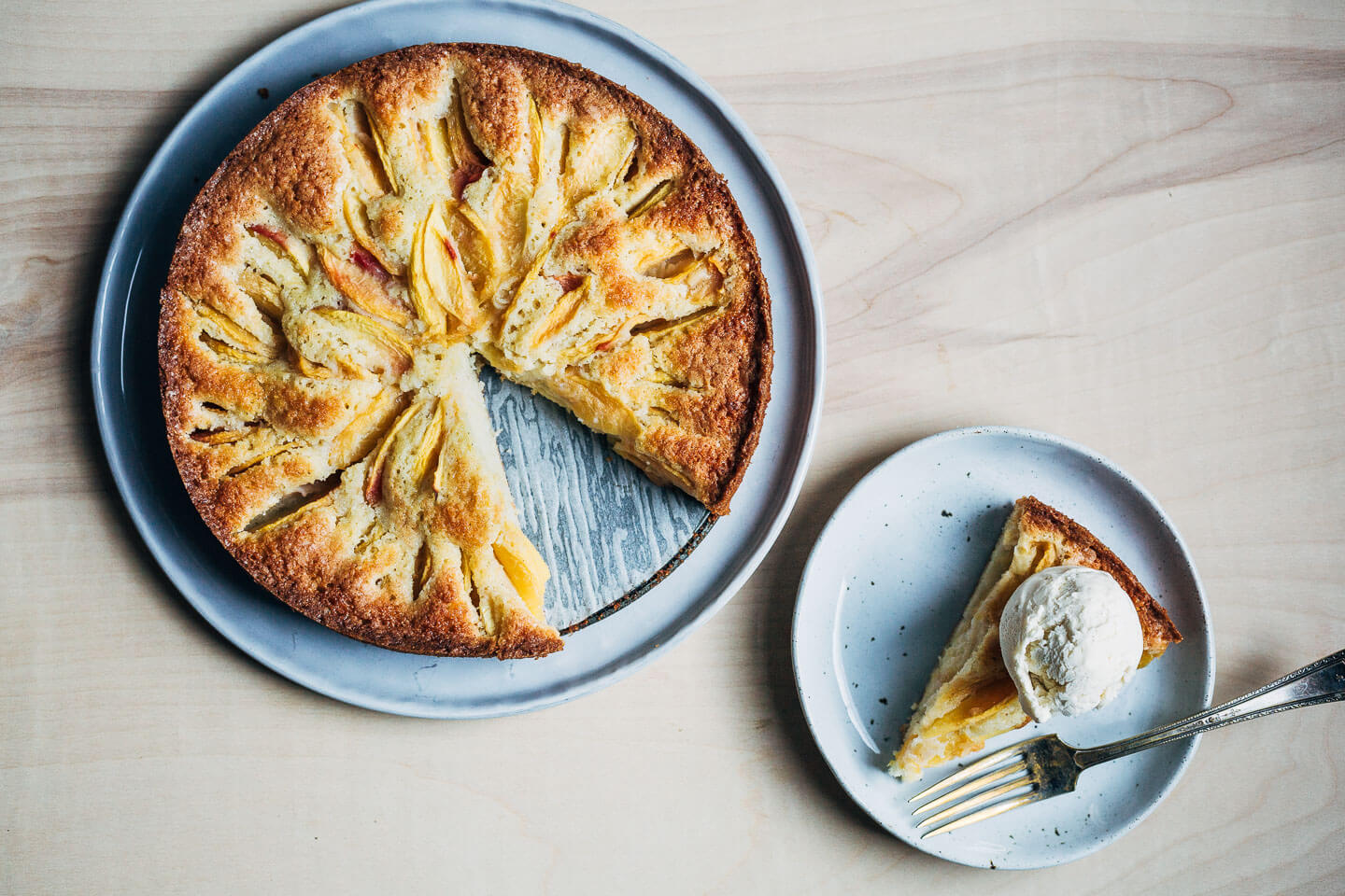 A peach cake with a slice removed and a slice alongside with a scoop of ice cream on top. 